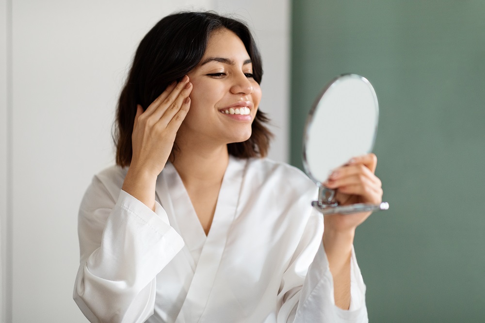 Frau-mit-schoener-Haut-durch-probiotische-Hautpflege-betrachtet-sich-im-Spiegel